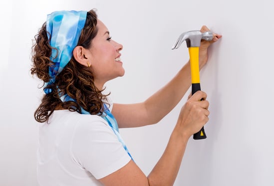 Casual woman hitting a nail in a wall with a hammer